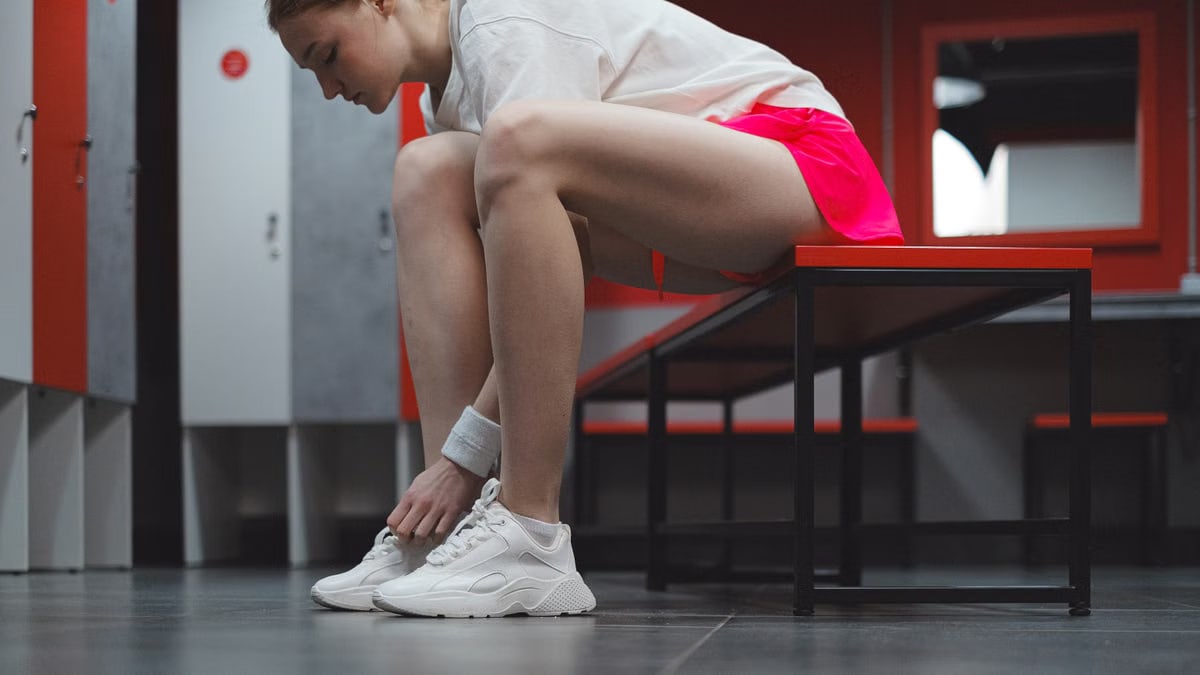 A woman in sportswear tying her shoes in a locker room, showing dedication to fitness.